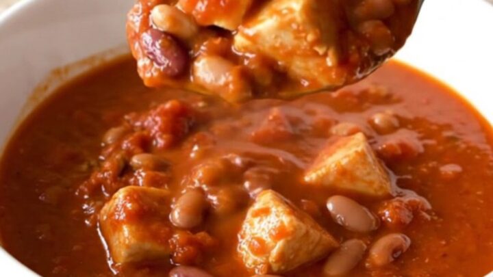 A close-up of a steaming bowl of three bean chicken chili in a white shallow bowl.