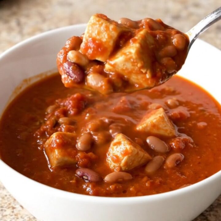 A close-up of a steaming bowl of three bean chicken chili in a white shallow bowl.
