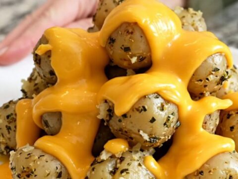 A close-up of tender halved baby red potatoes in a slow cooker topped with melted cheddar cheese and herbs.