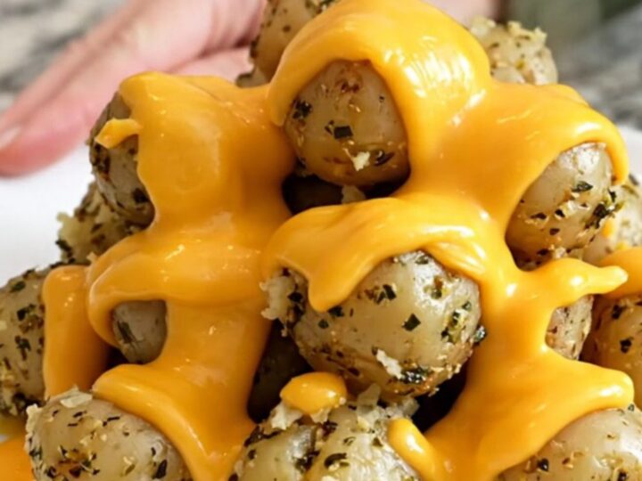 A close-up of tender halved baby red potatoes in a slow cooker topped with melted cheddar cheese and herbs.