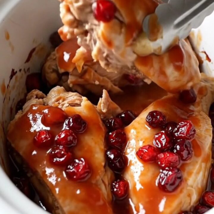 A top-down view of four raw chicken breasts placed in a slow cooker