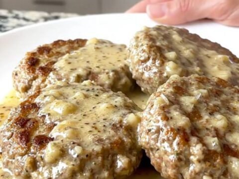 Close-up of slow cooked turkey burger steaks coated in a creamy white garlic parmesan sauce with visible herbs.