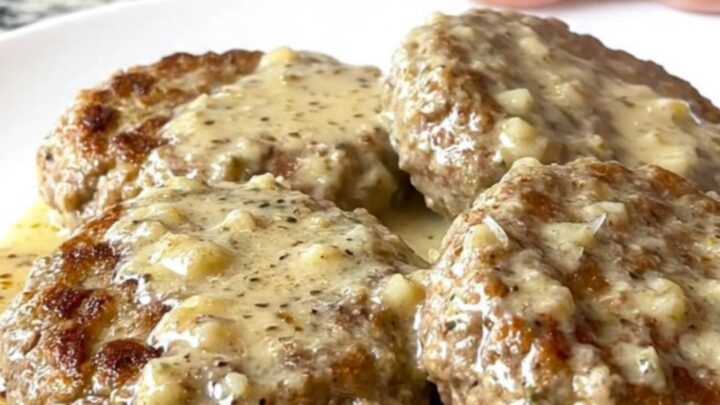 Close-up of slow cooked turkey burger steaks coated in a creamy white garlic parmesan sauce with visible herbs.