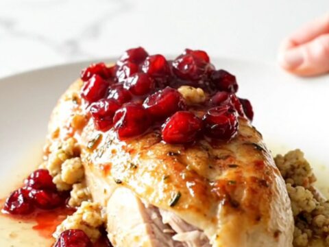 A ceramic slow cooker filled with cooked chicken breasts topped with cranberry sauce and herb stuffing.