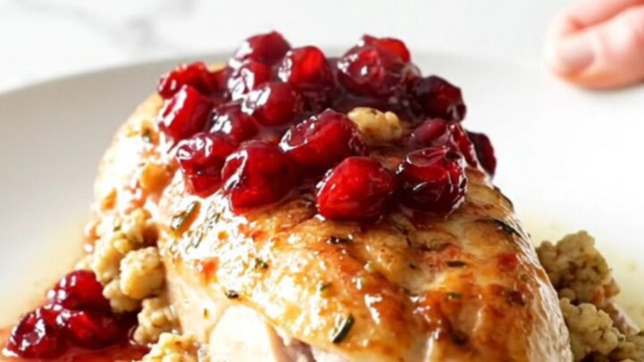 A ceramic slow cooker filled with cooked chicken breasts topped with cranberry sauce and herb stuffing.