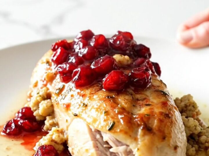 A ceramic slow cooker filled with cooked chicken breasts topped with cranberry sauce and herb stuffing.