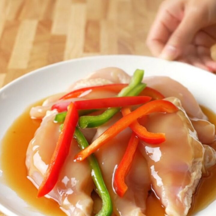 A white plate featuring tender honey pepper chicken strips surrounded by colorful bell pepper slices and a rich