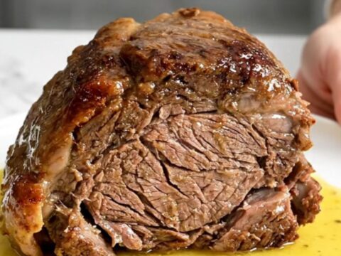 A slow cooker chuck roast served on a white plate with carrots and a rich, buttery lemon sauce.