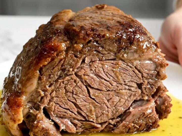 A slow cooker chuck roast served on a white plate with carrots and a rich, buttery lemon sauce.