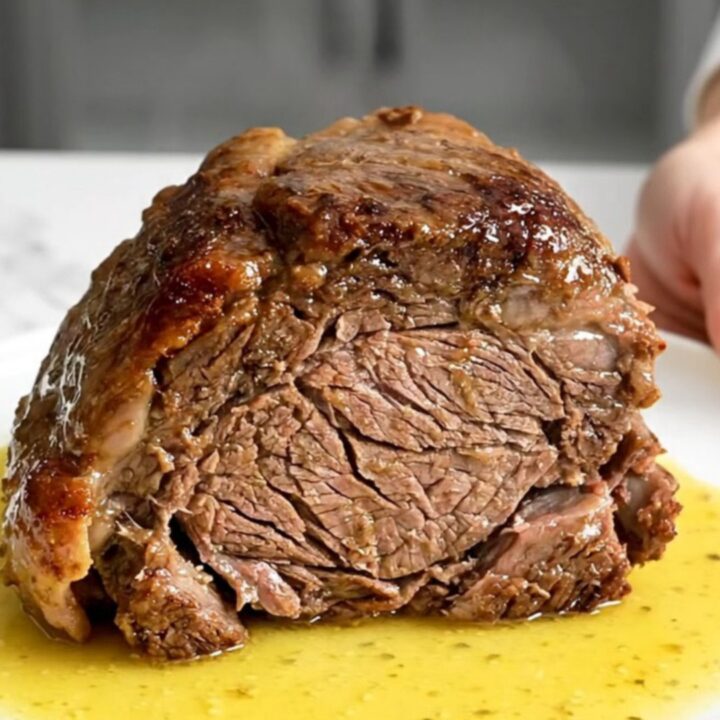 A slow cooker chuck roast served on a white plate with carrots and a rich, buttery lemon sauce.