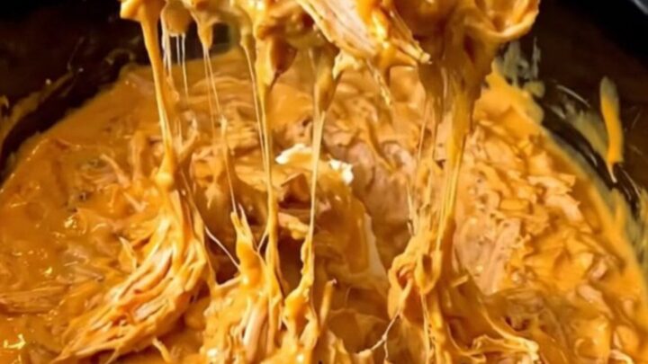 A close-up of a creamy, orange-red Nashville hot chicken dip in a black slow cooker insert.