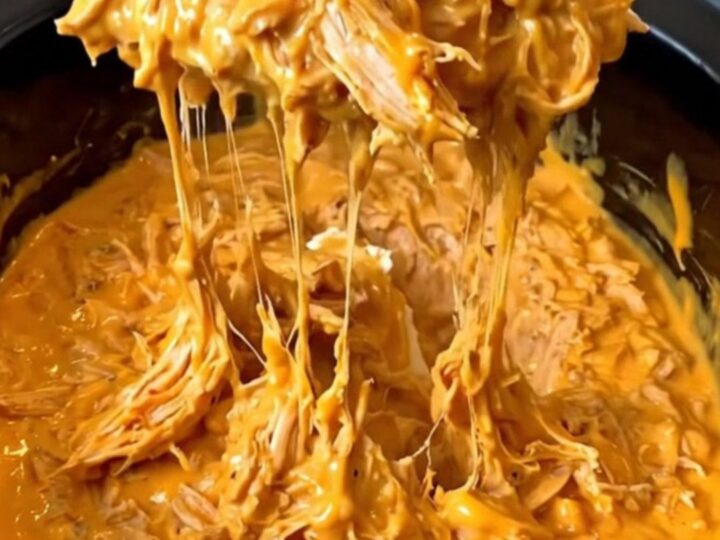 A close-up of a creamy, orange-red Nashville hot chicken dip in a black slow cooker insert.
