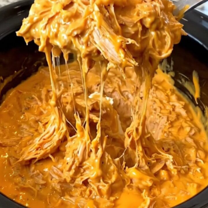 A close-up of a creamy, orange-red Nashville hot chicken dip in a black slow cooker insert.