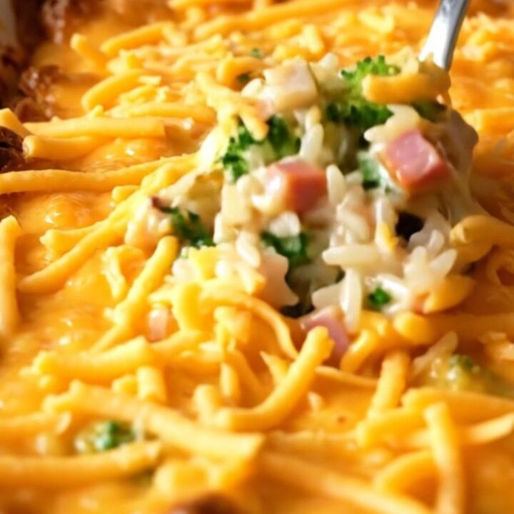 A top-down view of a rectangular ceramic dish filled with uncooked rice, diced ham, and fresh broccoli florets.