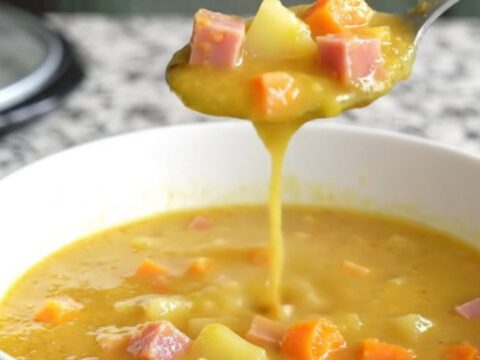 A bowl of creamy beer cheese soup with visible chunks of ham, gold potatoes, and carrots.