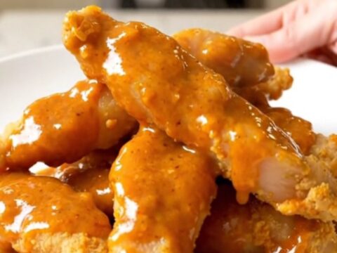 Slow cooker filled with cooked honey buffalo chicken tenders on a white countertop.