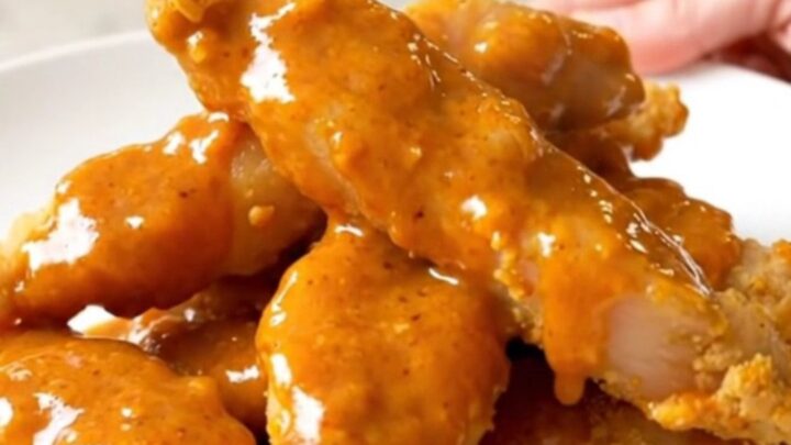 Slow cooker filled with cooked honey buffalo chicken tenders on a white countertop.
