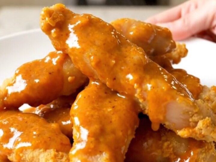 Slow cooker filled with cooked honey buffalo chicken tenders on a white countertop.