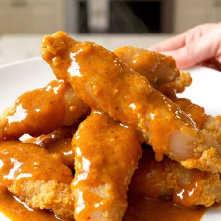 Slow cooker filled with cooked honey buffalo chicken tenders on a white countertop.