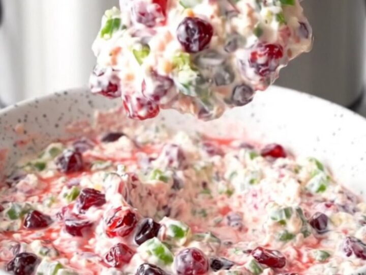 A slow cooker filled with creamy white cheese dip layered with green jalapenos and red cranberry sauce.
