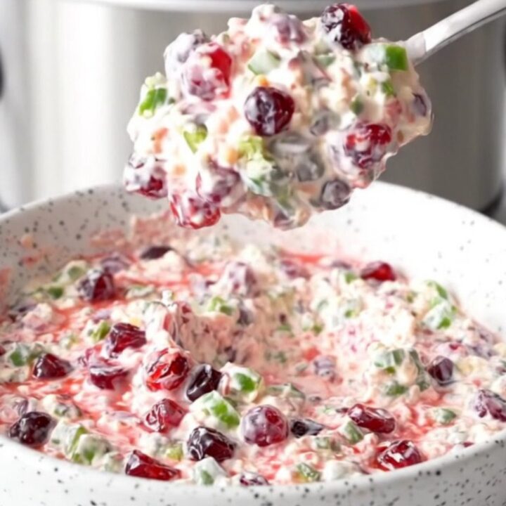 A slow cooker filled with creamy white cheese dip layered with green jalapenos and red cranberry sauce.