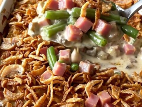 A golden, bubbly green bean and ham casserole in a ceramic dish topped with crispy fried onions.