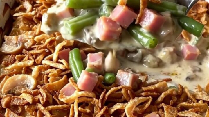 A golden, bubbly green bean and ham casserole in a ceramic dish topped with crispy fried onions.