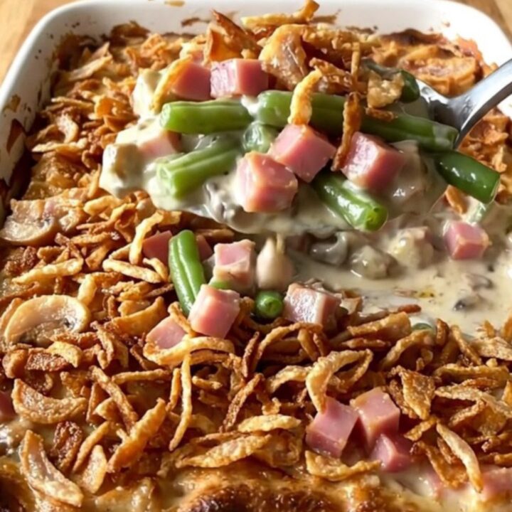 A golden, bubbly green bean and ham casserole in a ceramic dish topped with crispy fried onions.