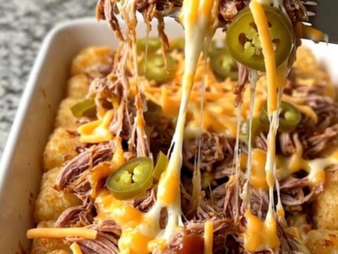 A top-down view of a ceramic dish filled with crispy potato tots, pulled pork, barbecue sauce, and melted cheddar cheese.