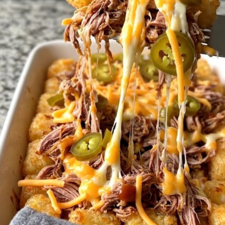 A top-down view of a ceramic dish filled with crispy potato tots, pulled pork, barbecue sauce, and melted cheddar cheese.