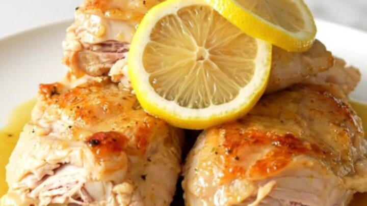 A close-up of tender, braised chicken thighs in a creamy, golden Dijon sauce with thin lemon slices.