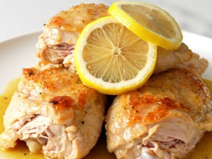 A close-up of tender, braised chicken thighs in a creamy, golden Dijon sauce with thin lemon slices.
