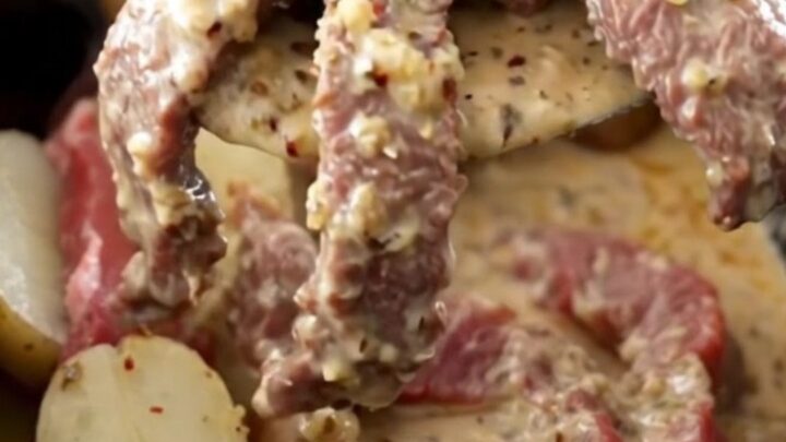 A close-up of tender round steak and baby red potatoes in a creamy garlic Parmesan sauce inside a slow cooker.
