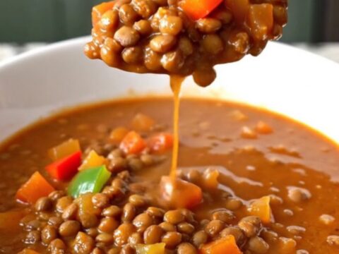A white shallow bowl filled with thick, hearty red-brown lentil chili on a kitchen counter.