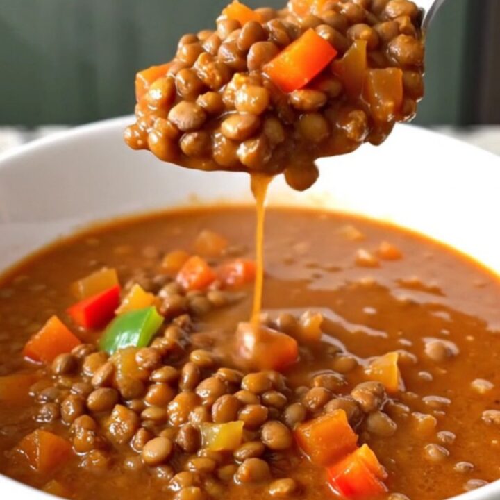 A white shallow bowl filled with thick, hearty red-brown lentil chili on a kitchen counter.