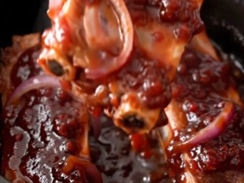 Slow cooker ribs coated in a dark, glossy raspberry barbecue sauce on a white plate.