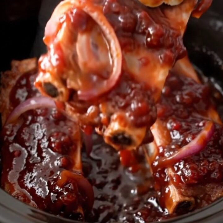 Slow cooker ribs coated in a dark, glossy raspberry barbecue sauce on a white plate.