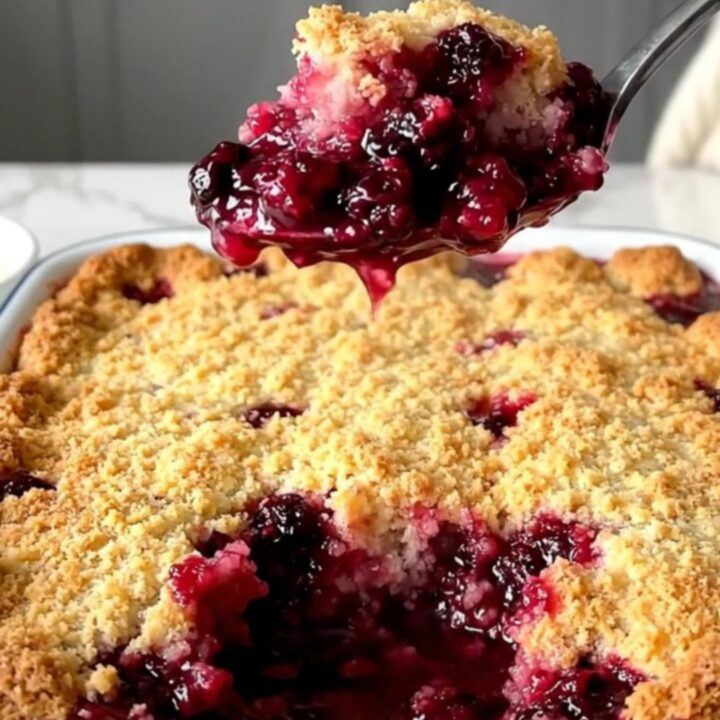 A top-down view of a golden, bubbling berry cobbler in a white rectangular baking dish on a quartz countertop.