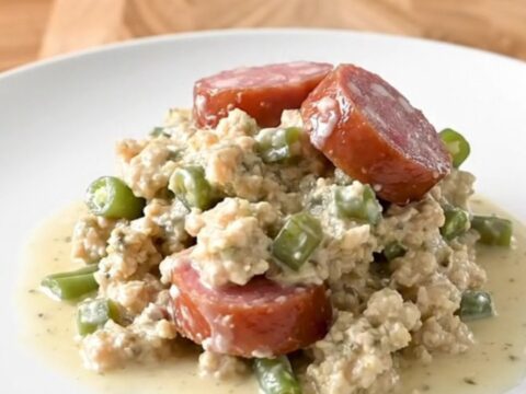 A slow cooker filled with layers of smoked sausage, green beans, and herb stuffing in a creamy sauce.