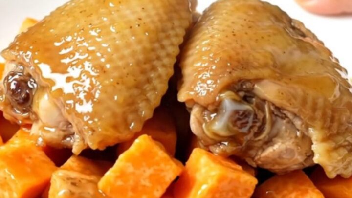 A top-down shot showing raw chicken thighs and sweet potato cubes inside a black slow cooker insert.