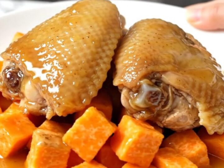 A top-down shot showing raw chicken thighs and sweet potato cubes inside a black slow cooker insert.