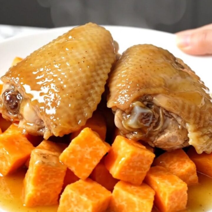 A top-down shot showing raw chicken thighs and sweet potato cubes inside a black slow cooker insert.