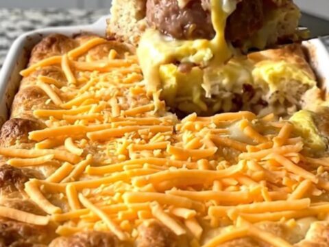 A golden, baked breakfast casserole in a white dish, featuring biscuit pieces, sausage, and melted cheese.