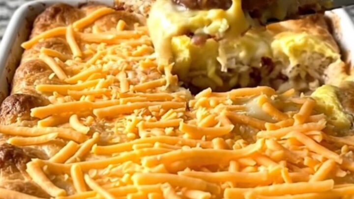 A golden, baked breakfast casserole in a white dish, featuring biscuit pieces, sausage, and melted cheese.