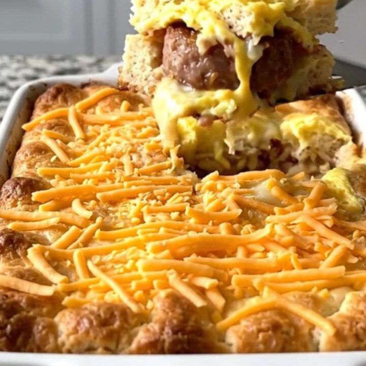 A golden, baked breakfast casserole in a white dish, featuring biscuit pieces, sausage, and melted cheese.
