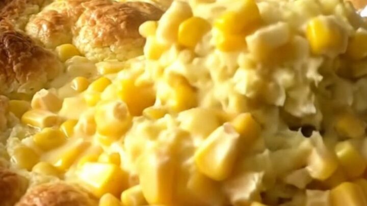 A golden, baked corn pudding in a white ceramic dish sitting on a speckled granite countertop.