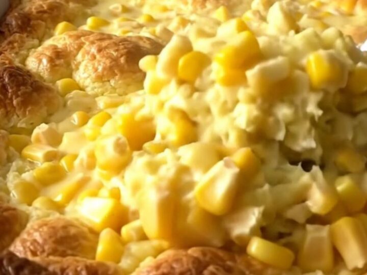 A golden, baked corn pudding in a white ceramic dish sitting on a speckled granite countertop.