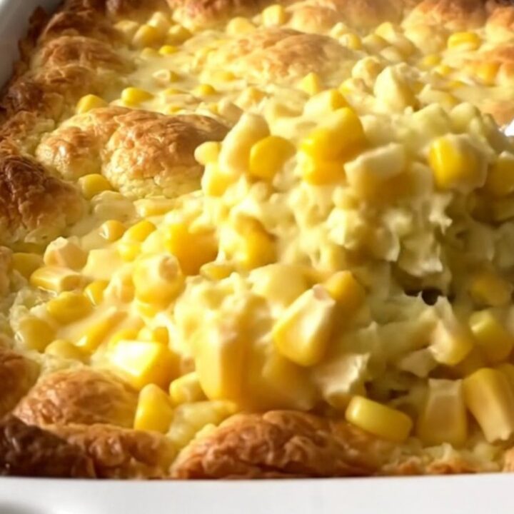 A golden, baked corn pudding in a white ceramic dish sitting on a speckled granite countertop.