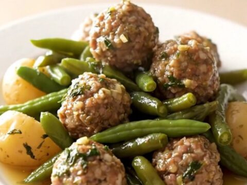 A close-up of tender beef meatballs with green beans and halved baby potatoes in a savory broth.