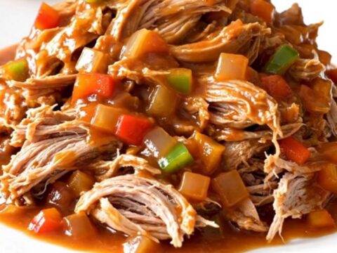 A close-up of tender, shredded pulled pork in a rich, dark red tomato sauce, served in a ceramic slow cooker.